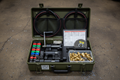 Steel ammo-can case open on shop floor showing manual hose crimper, die sets, fittings, hose lengths, and crimp spec chart